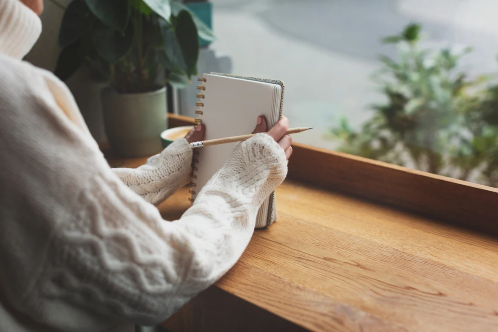 Unidentified woman is writing in the notepad in cafe. Working on bullet journal, diary, morning pages, plans and goals.