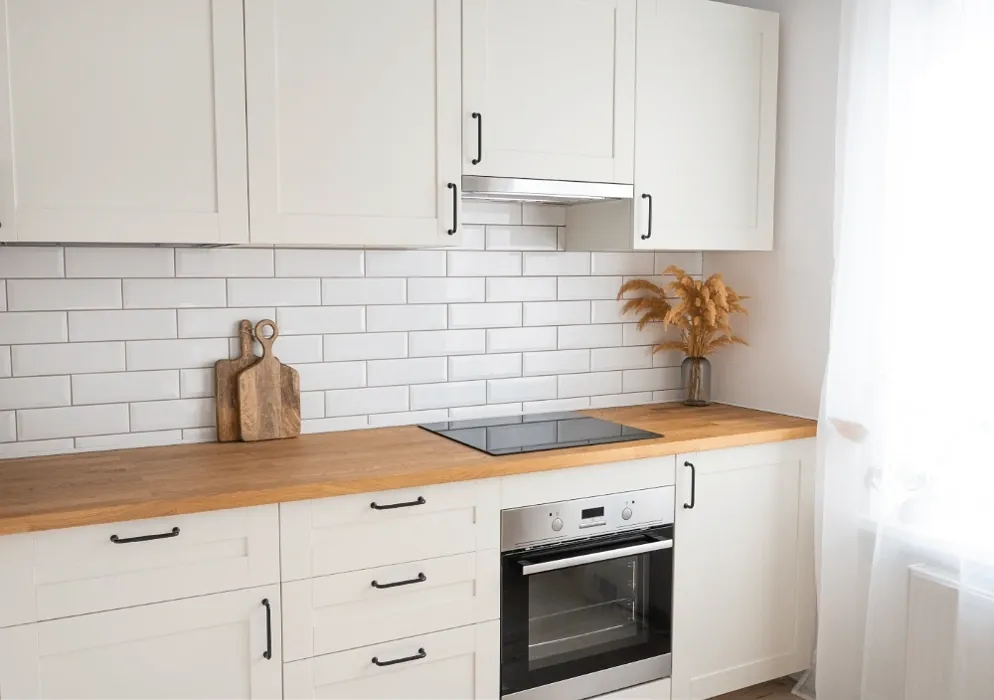 Wooden oak tabletop with a cup of tea and a kettle against the backdrop of a white kitchen with a brick wall with morning sunlight from the window.