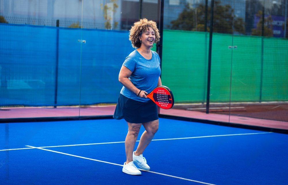 Middle age woman playing padel on outdoor court.